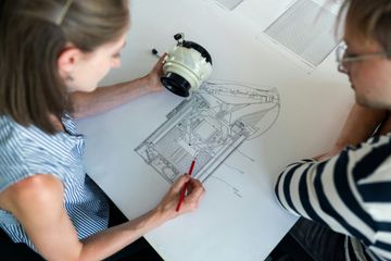 Two engineers discussing a technical drawing and component